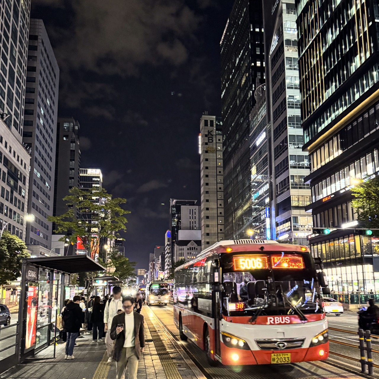 A red route 5006 bus and passengers at Gangnam Station’s central bus lane at night