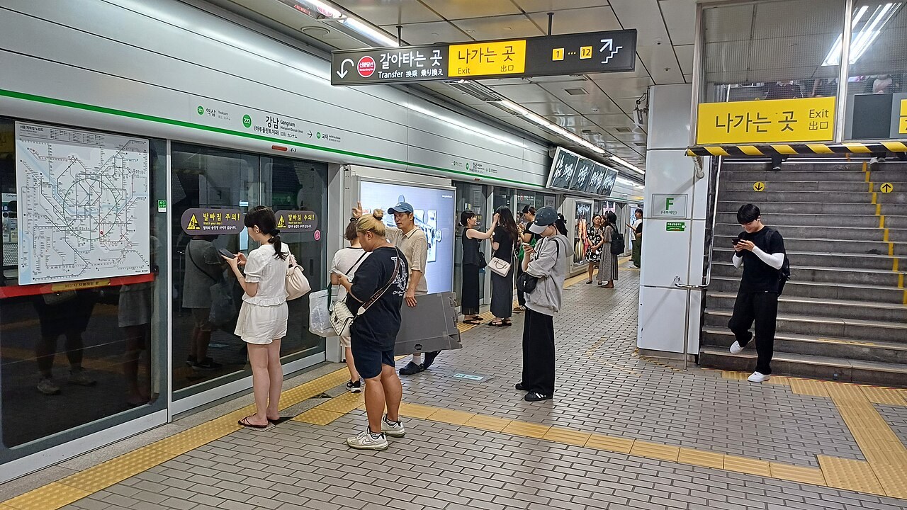 Passengers wait beside platform screen doors and bilingual exit signs at Gangnam Station on Seoul Subway Line 2